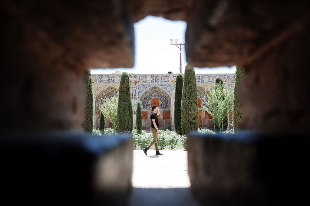 A man walking through a garden framed by stone arches